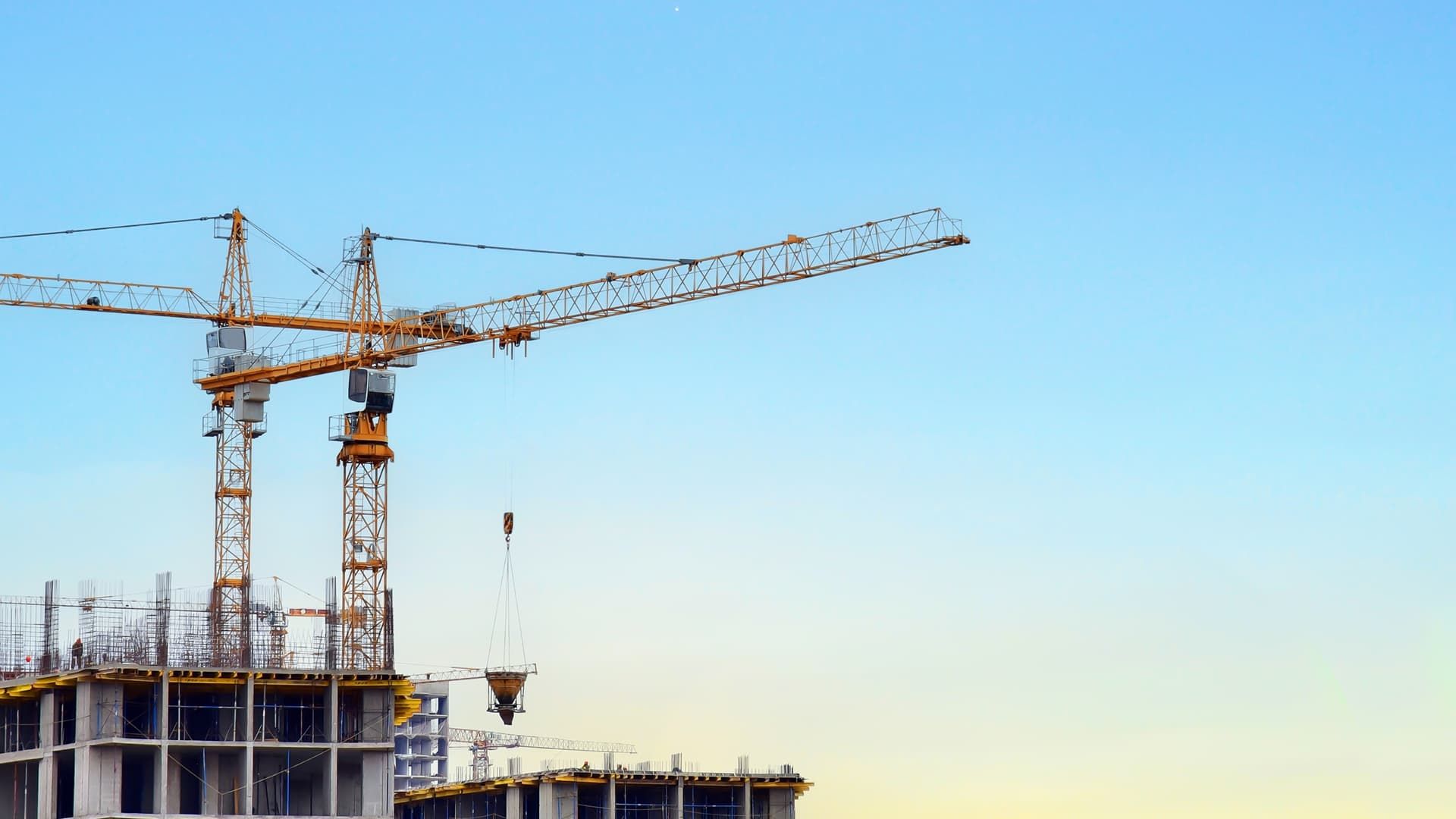 Baustelle mit zwei gelben Baukränen und Rohbau eines modernen Gebäudes vor blauem Himmel